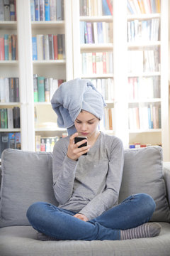 Girl wearing towel turban sitting on couch at home looking at cell phone