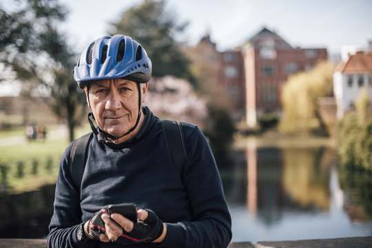 Portrait of senior man with cycling helmet using smartphone