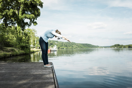 Woman on jetty wearing VR glasses pretending to dive into a lake