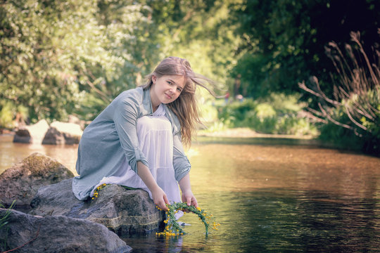 Blond girl on the lake with a wreath in her hands