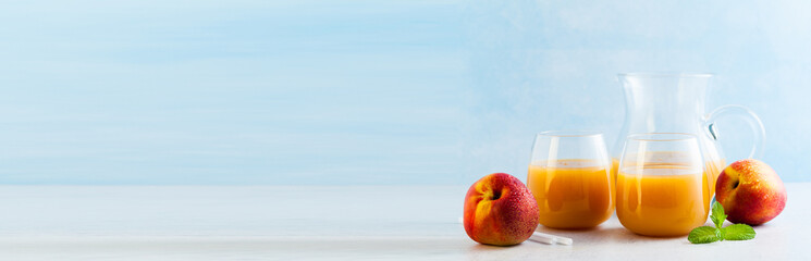 peach juice in glasses and a decanter and fresh peaches with leaves on a table. blue background. copy space