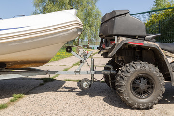 Transportation of inflatable boat on trailer. ATV quadbike moves ship to lake or river shore for launching. Beginning of water navigation and fishing season