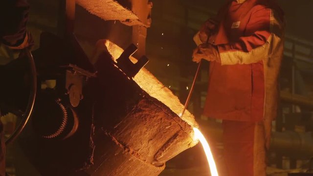 employee pours red hot molted metal from huge tank