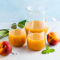 peach juice in glasses and a decanter and fresh peaches with leaves on a table. blue background. copy space