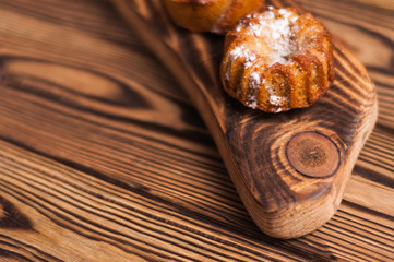 Row of baked cupcakes sprinkled powdered sugar on wooden cutting board on old rustic brown weathered table