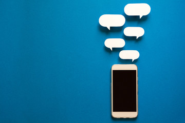 Smartphones with paper speech bubbles on blue background. Communication concept. Top view. Copy...