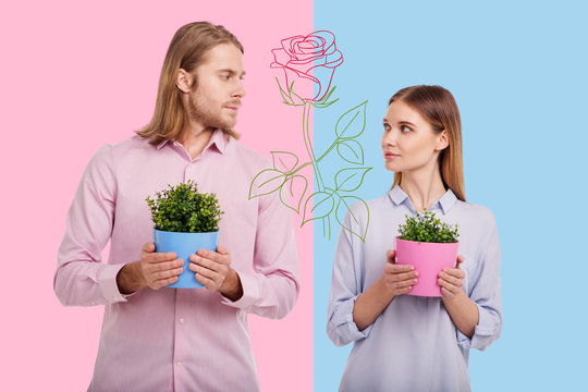 Loving plants. Romantic young couple looking at each other while being in their flower shop and holding colorful flower pots