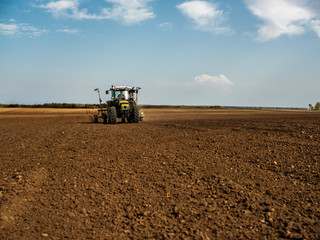 Fototapeta premium Farmer seeding, sowing crops at field. Sowing is the process of planting seeds in the ground as part of the early spring time agricultural activities.