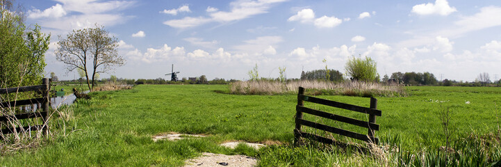 Typical dutch landscape with windmill, green grass, wooden fence, blue sky, white clouds and trees