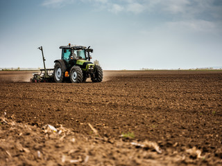 Fototapeta premium Farmer seeding, sowing crops at field. Sowing is the process of planting seeds in the ground as part of the early spring time agricultural activities.