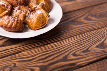 Baked cupcakes sprinkled powdered sugar on white ceramic dish on old rustic brown weathered table