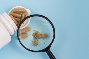 Organic pills in a medical jar seen from a magnifying glass on blue background. With copy space