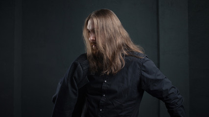 Portrait of man with long hair and beard in black clothes on dark background