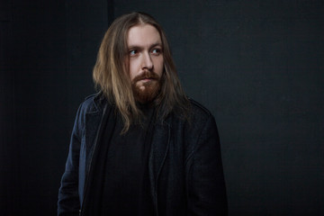 Portrait of man with long hair and beard in black clothes on dark background
