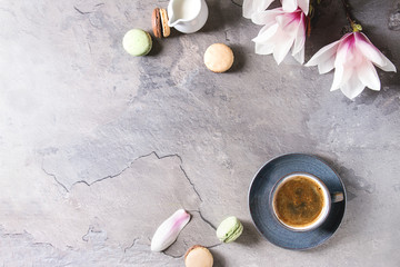 Obraz na płótnie Canvas Blue cup of black espresso coffee with french dessert macaroons, cream and spring flowers magnolia branches over grey texture background. Top view, space. Spring greeting card, wallpapers