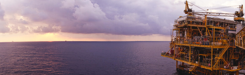 Offshore oil and gas rig platform with beautiful sunset time with storm of clouds in the gulf of Thailand for business industrial concept panorama view