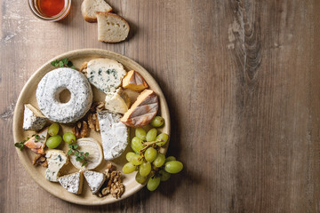 Cheese plate assortment of french cheese served with honey, walnuts, bread and grapes on ceramic plate over wood texture background. Top view, copy space.