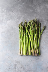 Raw uncooked organic green asparagus in row over grey texture background. Top view, copy space.