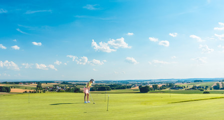 Full length of a determined young woman practicing golf moves and strikes on the grass of a training area for putting green, in an idyllic sunny rural place