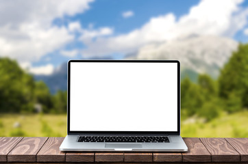 Modern laptop with empty white screen on wooden table against blurred mountains background