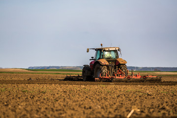 Fototapeta premium Farmer in tractor preparing land with seedbed cultivator as part of pre seeding activities in early spring season of agricultural works at farmlands.