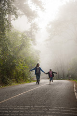 A little girl and mother run on a road in the forest