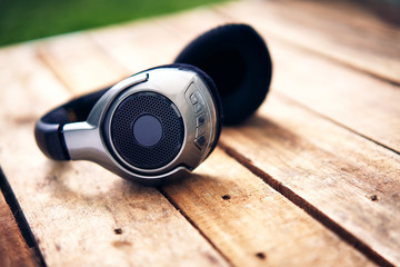 A 45 degree view of a set of wireless headphones lying on a rustic wooden table outside. Styling and grain effect added to image.