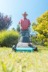 Low-angle view of an active senior man smiling and looking at camera while using a grass cutting machine in the garden