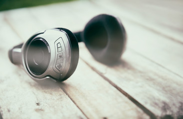A 45 degree view of a set of wireless headphones lying on a rustic wooden table outside. Styling and grain effect added to image.