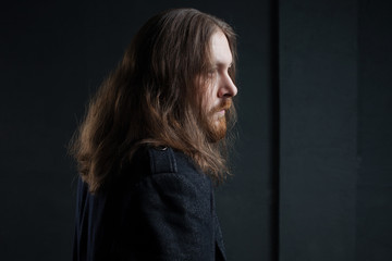 Portrait of man with long hair and beard in black clothes on dark background