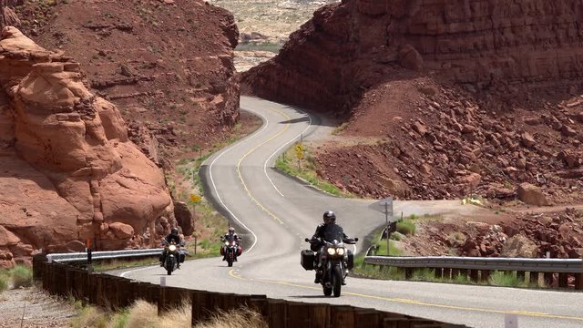Motorcyclists driving in winding road in Utah cutting through the desert landscape.
