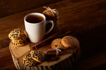 Christmas concept with a cup of hot tea, cookies and decorations on a log over wooden background, selective focus