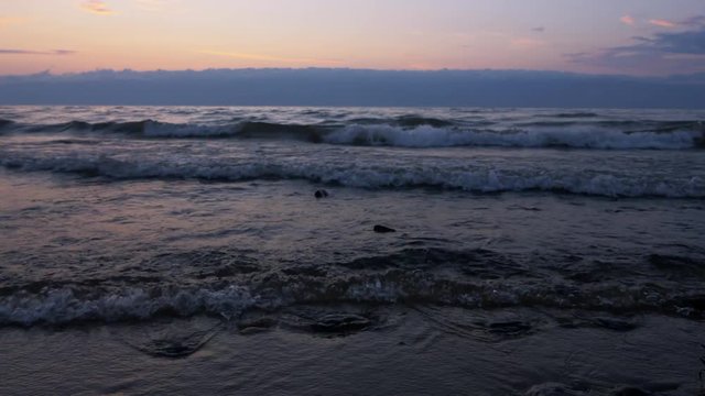 Beautiful sunset on the sea coast. The camera looks down on the bars. Waves are beautiful and soft washed by the sandy beach.