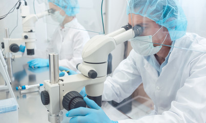 Two lab technicians or scientists working in laboratory looking thru microscopes 