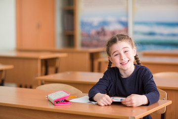 child girl sits at the Desk in the classroom, looks in the frame and smiling
