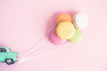 Macarons in form of balloons attached to small retro car with strings.