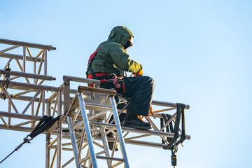 Naklejka na ściany i meble Industrial climber in uniform sitting ts on a building structure