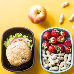 Lunch for a child who is in school with them. Sandwich, strawberries and peanuts in plastic boxes. Next to the apple. Top view, flat lay