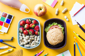 School supplies of the child and lunch in plastic boxes on a yellow background. Healthy food for a child to take to school concept. Top view, flat lay