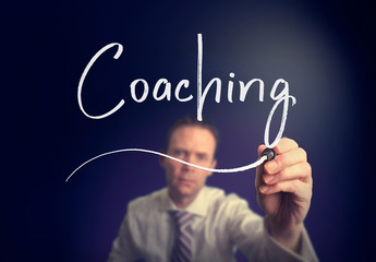 A businessman writing a Coaching concept with a white pen on a clear screen.