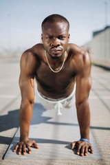 African American man stands on his arms on the ground doing push-ups during his morning exercises