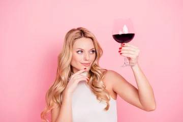 Keuken foto achterwand Alcohol Portret van nadenkend, deskundige, elegante mooie vriendin kijken naar verhoogd glas met alcohol drinken in de hand met evaluatieve weergave geïsoleerd op roze achtergrond