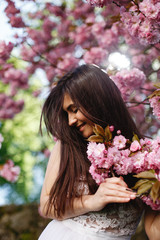 Fototapeta premium Wind blows brunette woman's hair while she poses before a blooming sakura tree