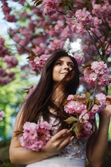 Wind blows brunette woman's hair while she poses before a blooming sakura tree
