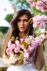 Wind blows brunette woman's hair while she poses before a blooming sakura tree