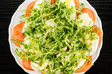 Caprese salad  flatlay on a plate isolated on black wooden background.