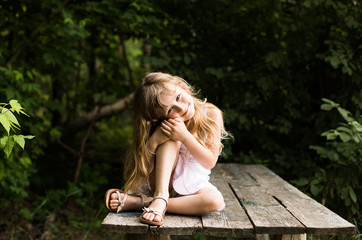 Pretty smiling pensive girl sitting on the old bridge in the forest
