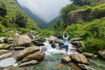 Woman in yoga asana Vrikshasana tree pose at waterfall outdoors