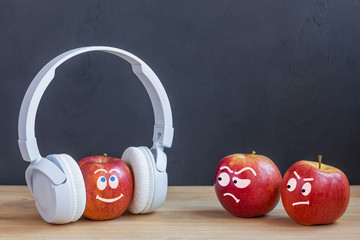 One apple in wireless headphones listening to music, two apple envy him. music concept. psychology of attitude - obrazy, fototapety, plakaty