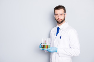 Portrait with copy space, empty place of attractive stylish  scientist with bristle in white lab coat, tie holding test tubes with multi-colored liquid, looking at camera over grey background
